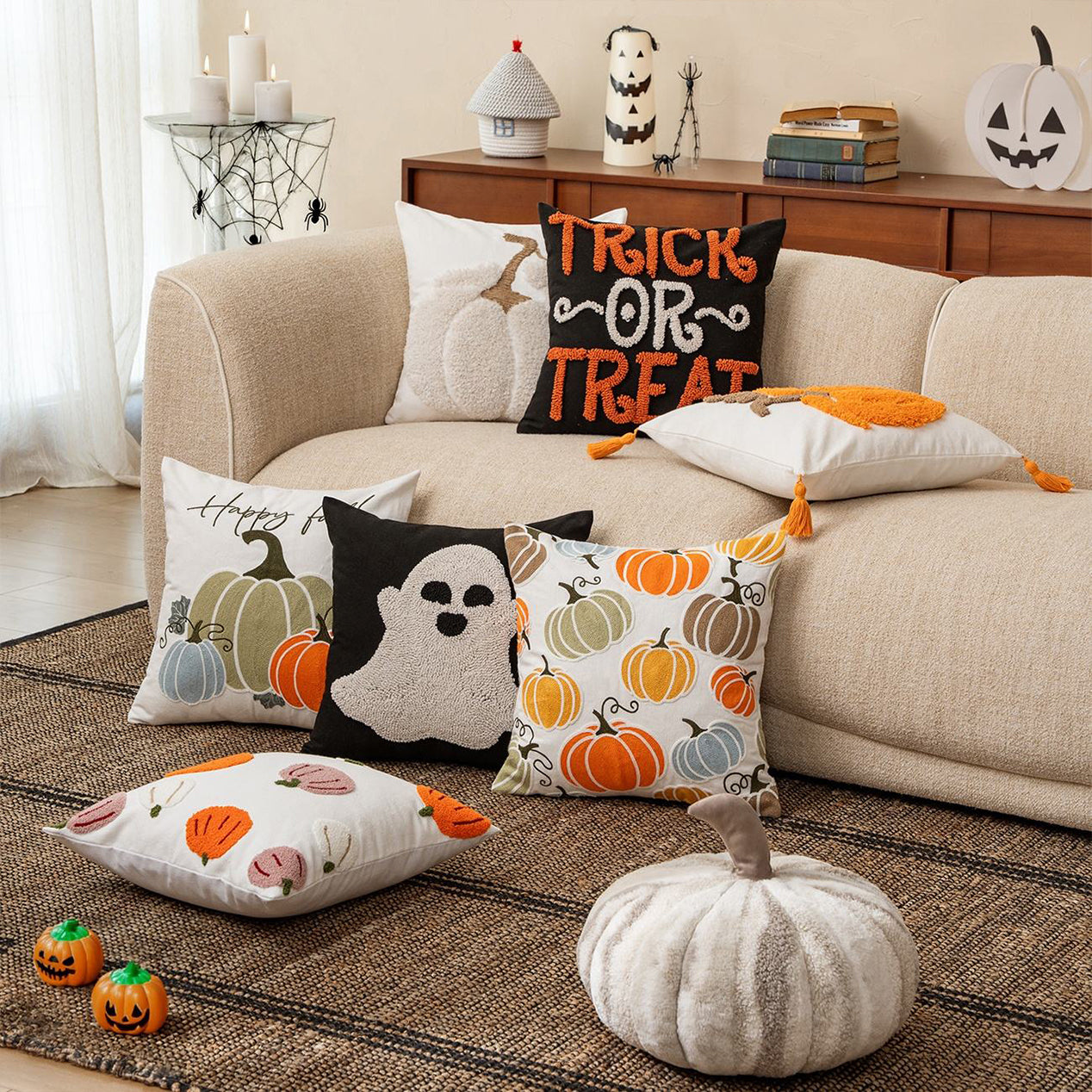 Halloween-themed pillows on a beige sofa with decorative pumpkins on a brown rug.